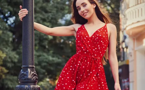 Junge Frau in einem roten Kleid mit Polka Dot Muster lehnt an einer Laterne.