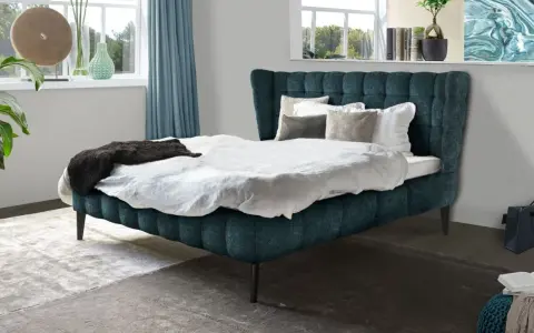 Ein luxuriöses Bett mit tiefblauem Polster und weißen Bettwäsche-Ideen. Dekorative Kissen und eine dunkle Decke laden zum Entspannen ein.