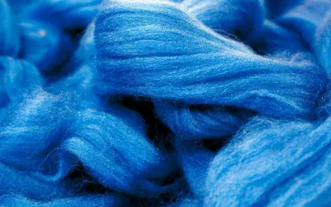 Leuchtend blaue Fasern, die an Wolle erinnern. Obwohl sie sich wie eine Naturfaser anfühlt, ist Viskose eine künstlich hergestellte Faser.