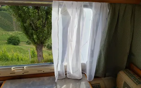 Leichte, transparente **Wohnwagen Gardinen Ideen** mit bunten Fäden vor einem Fenster mit Blick auf Weinberge.