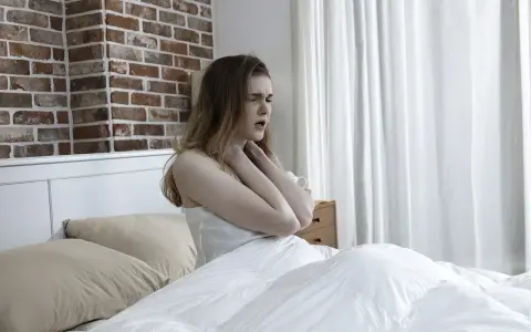 Junge Frau im Bett, die sich die Kehle hält, als ob das **Bett quietscht** und sie stört.