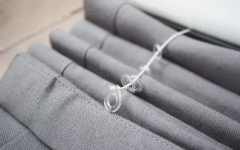 Grauer Raffrollo Stoff mit Schnüren und Ringen, bereit zum Raffrollo waschen.