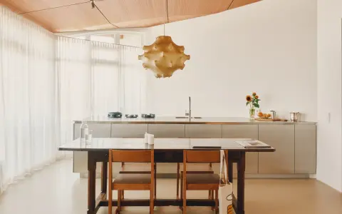 Ein Essbereich mit Holztisch und Stühlen, der den schwedischen Wohnstil verkörpert. Dahinter eine moderne Küche mit Edelstahlfronten und eine auffällige Hängelampe.