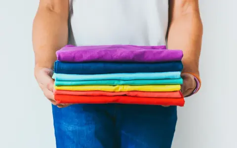 Ein Stapel bunter GSM Kleidung, gehalten von Händen in Jeans.