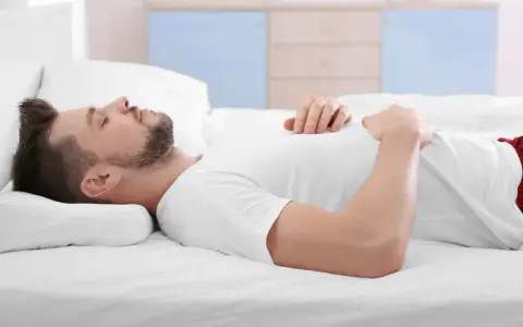 Mann schläft auf dem Rücken, Kopf auf einem Kissen gebettet. Die richtige Schlafposition mit dem passenden Kissen ist wichtig für erholsamen Schlaf.