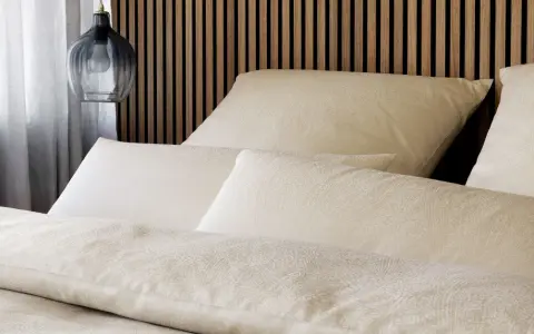 Gemütliches Bett mit Kissen und Decken im dezenten **muster paisley**. Ein moderner Nachttischlampen-Pendel hängt daneben.