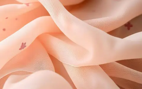 Zartes, pfirsichfarbenes Mesh-Textil mit kleinen, roten Herzchen-Mustern, das sanft fällt und glänzt.