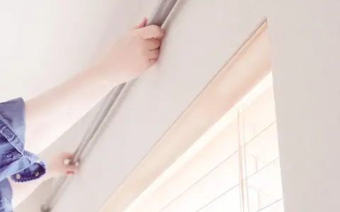 Hände befestigen eine Gardinenschiene an der Decke ohne Bohren. Einfache Montage für Ihre Fensterdekoration.