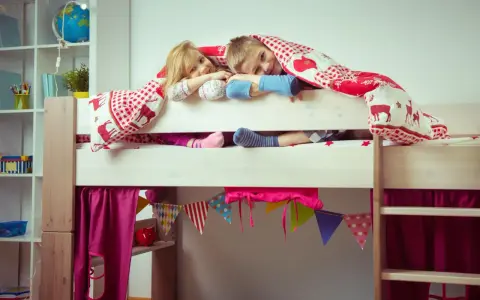 Zwei Kinder kuscheln sich unter einer Decke auf einem Hochbett. Die Frage "Hochbett ab wann?" stellt sich hier nicht, die Kleinen sind begeistert!