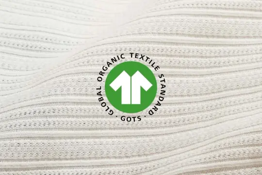 Das GOTS-Zertifikat auf weißem, geripptem Stoff. Es steht für Global Organic Textile Standard und garantiert nachhaltige Textilien.