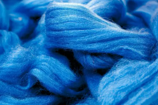 Leuchtend blaue Fasern, die an Wolle erinnern. Obwohl sie sich wie eine Naturfaser anfühlt, ist Viskose eine künstlich hergestellte Faser.