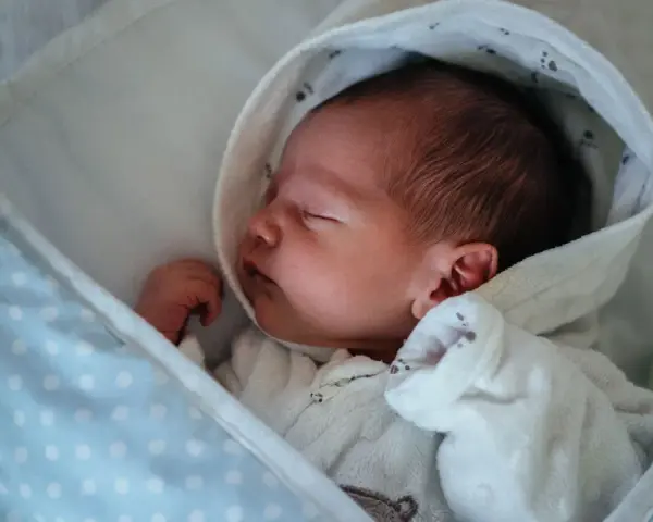 Neugeborenes Baby schläft friedlich, eingewickelt in eine Decke. Der sanfte "white noise" des Geräuschs hilft ihm beim Einschlafen.