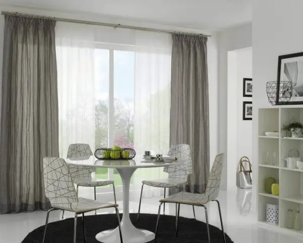 Ein Essbereich mit einem runden Tisch, vier Stühlen und einem Fenster, das von einer Gardinenschiene oder Stange mit grauen und weißen Vorhängen eingerahmt wird.