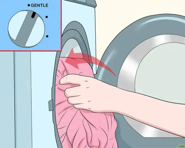 Hand lädt rosa Kleidung in die Waschmaschine. Das Programm "Sanft" ist ausgewählt, damit Viskose richtig gewaschen wird.