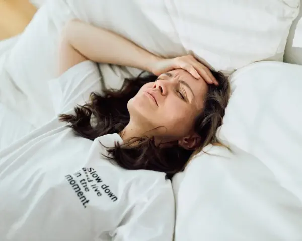 Frau liegt im Bett, Stirn gerunzelt, Hand an der Schläfe. Zu viele Gedanken im Kopf, kein Schlaf möglich.