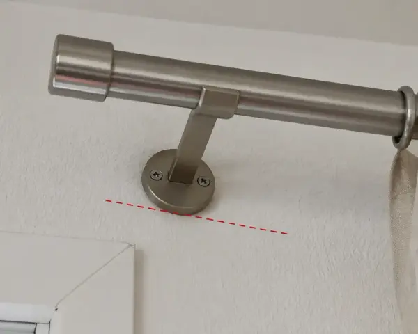 Eine Gardinenstange wird an der Wand befestigt, knapp unterhalb des Rolladenkastens. Die Halterung ist schräg montiert.