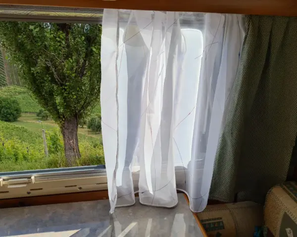 Leichte, transparente **Wohnwagen Gardinen Ideen** mit bunten Fäden vor einem Fenster mit Blick auf Weinberge.