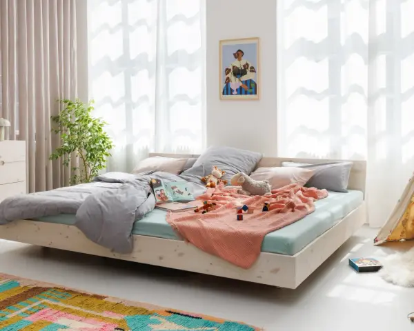 Ein gemütliches Familienbett mit Spielzeug und Kuscheltieren, das zum Kuscheln einlädt. Hier ist Platz für die ganze Familie.