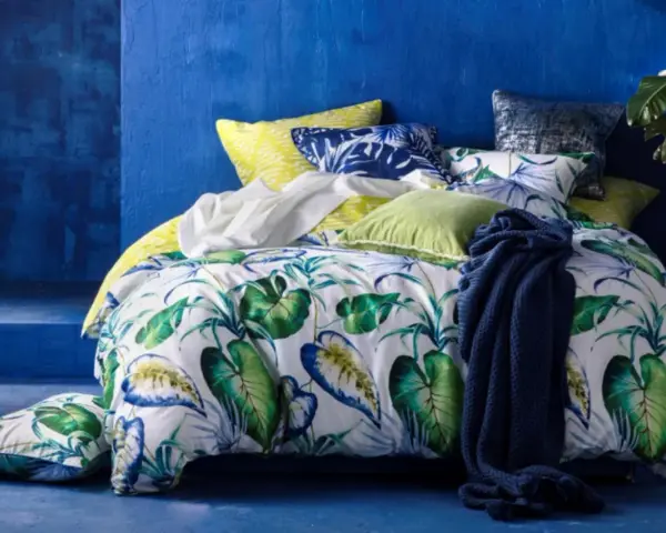 Ein tropisch gemustertes Bett mit Kissen in Blau und Grün. Für ein frisches Gefühl: wie oft Bettdecke wechseln?