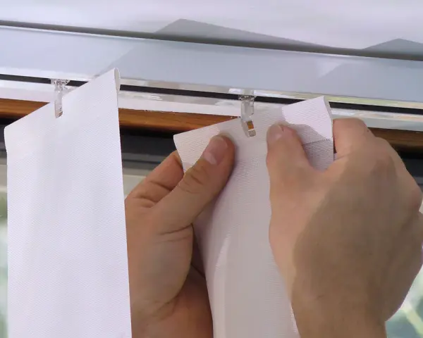 Hände befestigen einen Lamellenvorhang in einer Gardinenschiene mit Clips.