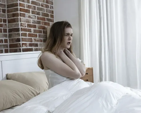 Junge Frau im Bett, die sich die Kehle hält, als ob das **Bett quietscht** und sie stört.