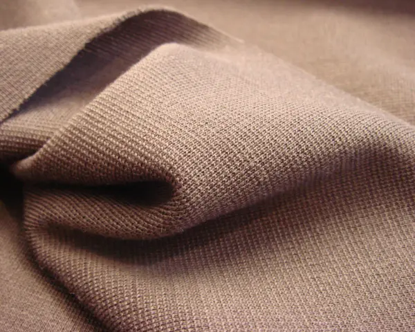 Braune Stofffalten, die die glatte, feine Struktur von Single Jersey zeigen. Dieses Material ist weich und dehnbar.