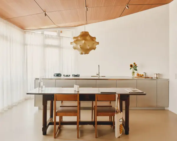 Ein Essbereich mit Holztisch und Stühlen, der den schwedischen Wohnstil verkörpert. Dahinter eine moderne Küche mit Edelstahlfronten und eine auffällige Hängelampe.