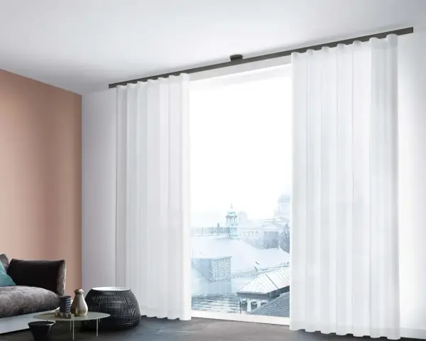 Weiße, transparente Vorhänge mit sanften Wellen und Falten rahmen ein Fenster mit Blick auf eine Stadtkulisse ein.