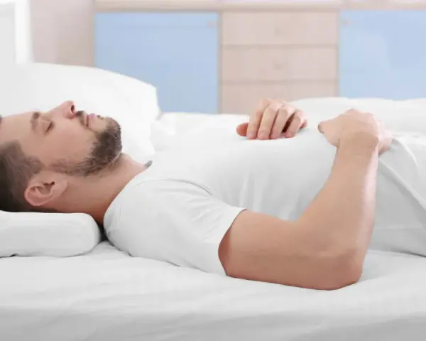 Mann schläft auf dem Rücken, Kopf auf einem Kissen gebettet. Die richtige Schlafposition mit dem passenden Kissen ist wichtig für erholsamen Schlaf.