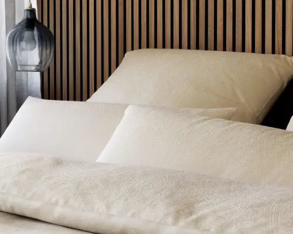 Gemütliches Bett mit Kissen und Decken im dezenten **muster paisley**. Ein moderner Nachttischlampen-Pendel hängt daneben.