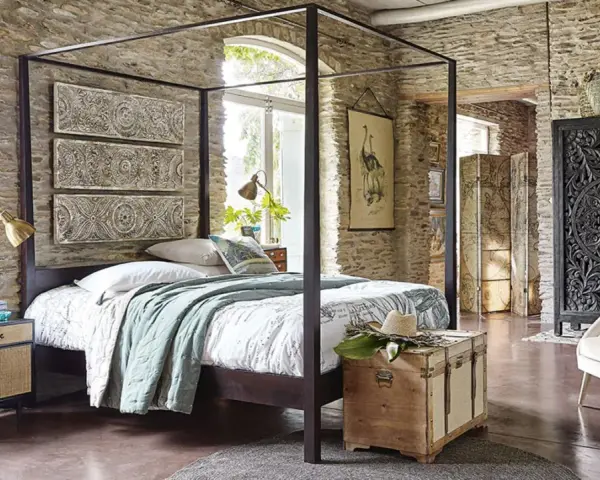 Ein Schlafzimmer mit Steinwänden und einem Himmelbett. Drei Wandpaneele mit orientalischen Mustern hängen über dem Bett. Ein Holztruhe steht am Fußende.