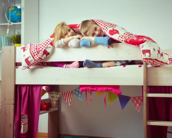 Zwei Kinder kuscheln sich unter einer Decke auf einem Hochbett. Die Frage "Hochbett ab wann?" stellt sich hier nicht, die Kleinen sind begeistert!
