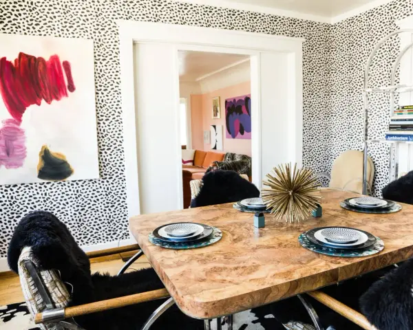 Esszimmer mit auffälliger Tapete im Jaguar Muster. Ein Holztisch mit Tellern und ein Kunstwerk an der Wand.
