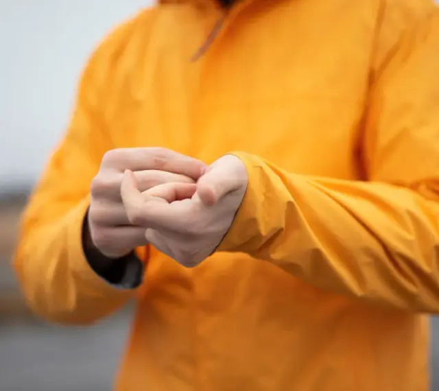 Person reibt sich die Hände unter einer leuchtend orangen Jacke. Ist Polyester warm? Ja, diese Jacke hält warm.