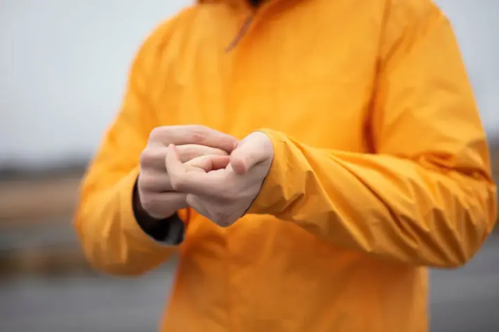 Person reibt sich die Hände unter einer leuchtend orangen Jacke. Ist Polyester warm? Ja, diese Jacke hält warm.