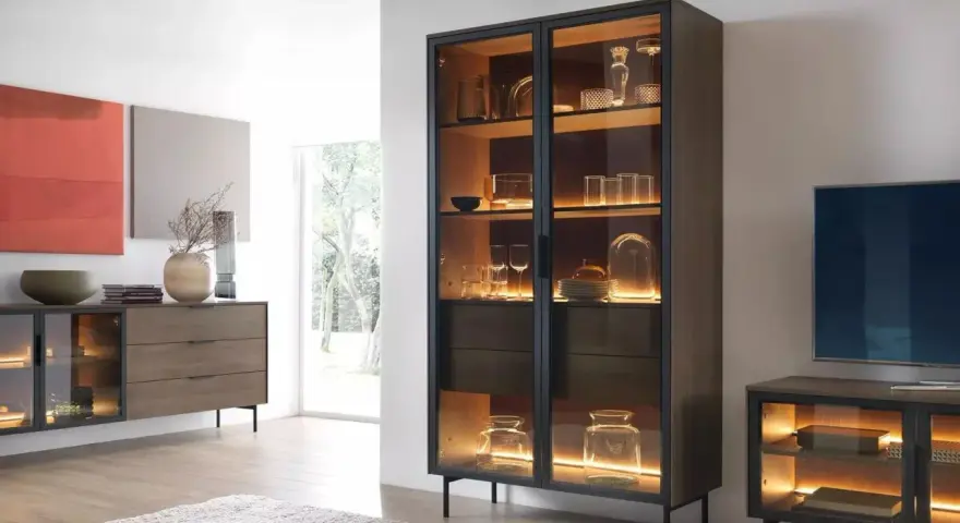 Beleuchteter Vitrinenschrank mit Gläsern und Dekoartikeln, daneben ein Sideboard.