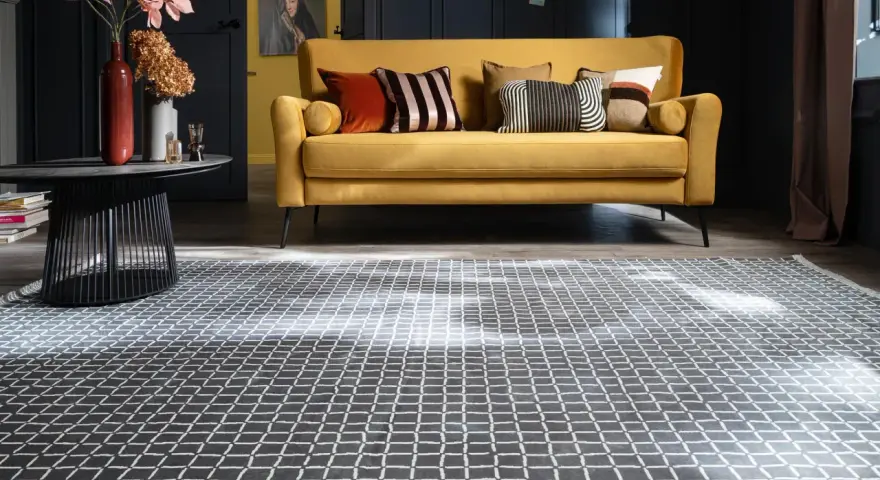 Ein gelbes Sofa mit Kissen steht auf einem gemusterten Teppich unter dem Sofa.