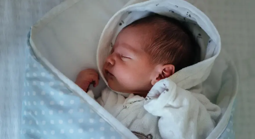 Neugeborenes Baby schläft friedlich, eingewickelt in eine Decke. Der sanfte "white noise" des Geräuschs hilft ihm beim Einschlafen.
