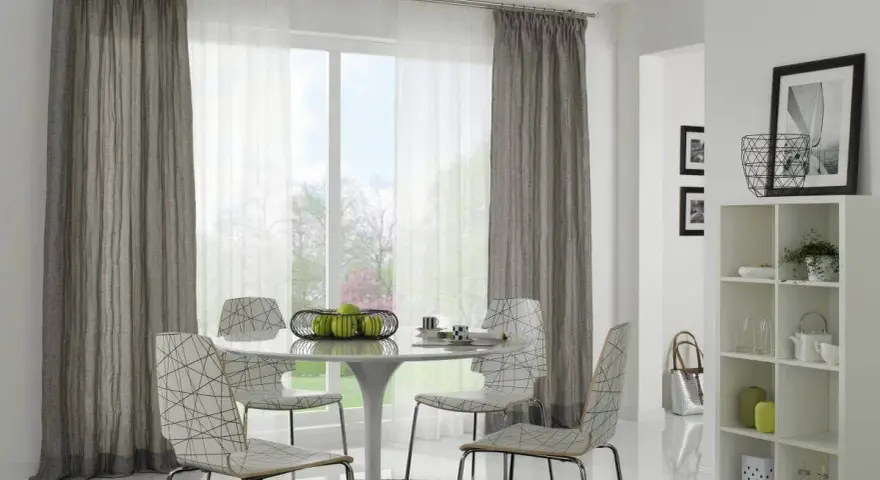 Ein Essbereich mit einem runden Tisch, vier Stühlen und einem Fenster, das von einer Gardinenschiene oder Stange mit grauen und weißen Vorhängen eingerahmt wird.