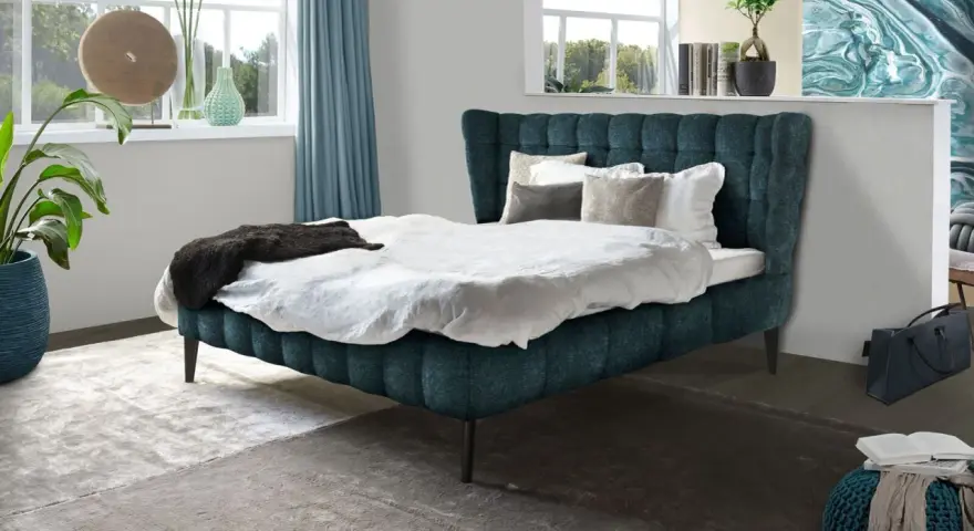 Ein luxuriöses Bett mit tiefblauem Polster und weißen Bettwäsche-Ideen. Dekorative Kissen und eine dunkle Decke laden zum Entspannen ein.