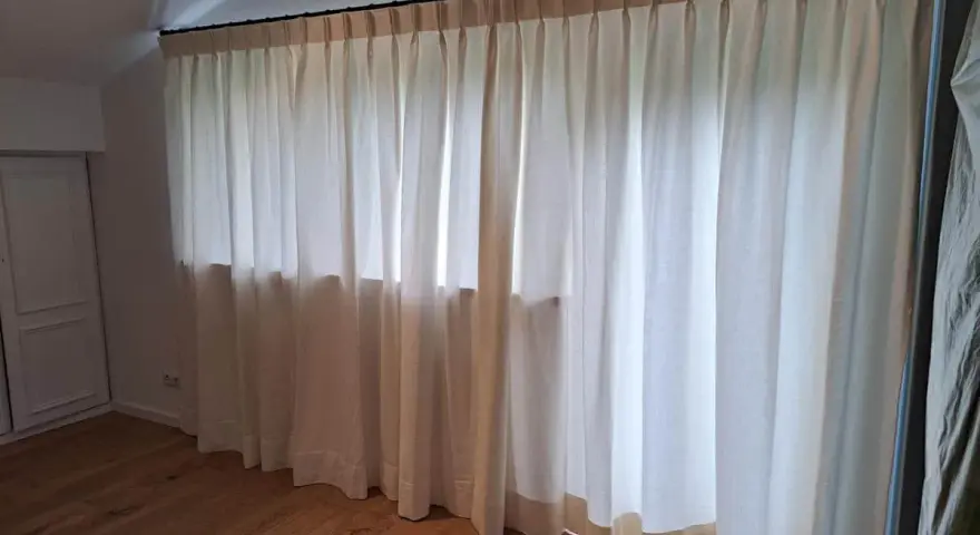 Neue Gardinen falten entfernen: Helle Stoffbahnen mit Faltenwurf hängen von einer Stange.