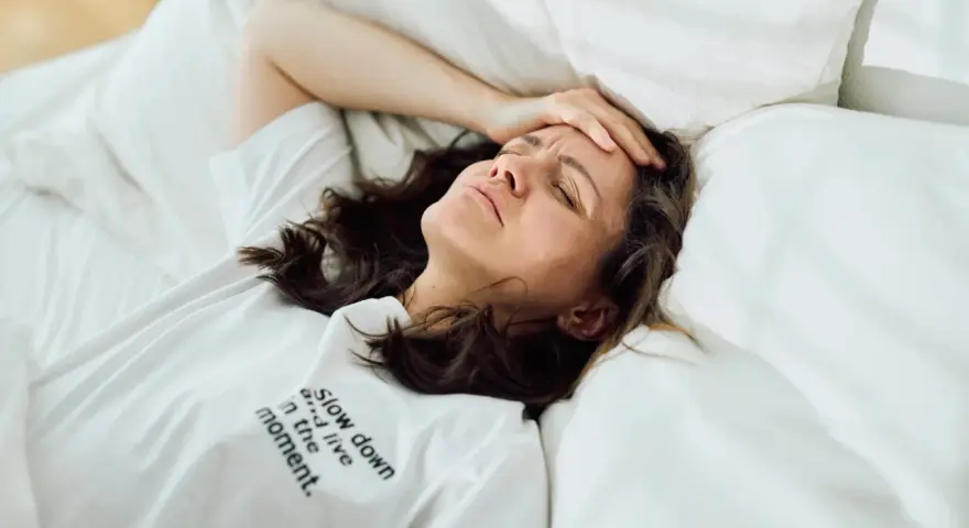 Frau liegt im Bett, Stirn gerunzelt, Hand an der Schläfe. Zu viele Gedanken im Kopf, kein Schlaf möglich.