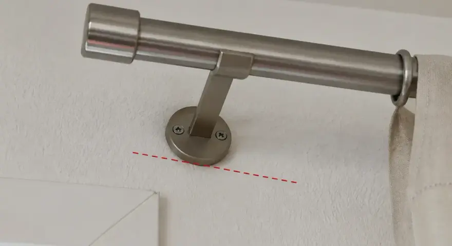 Eine Gardinenstange wird an der Wand befestigt, knapp unterhalb des Rolladenkastens. Die Halterung ist schräg montiert.