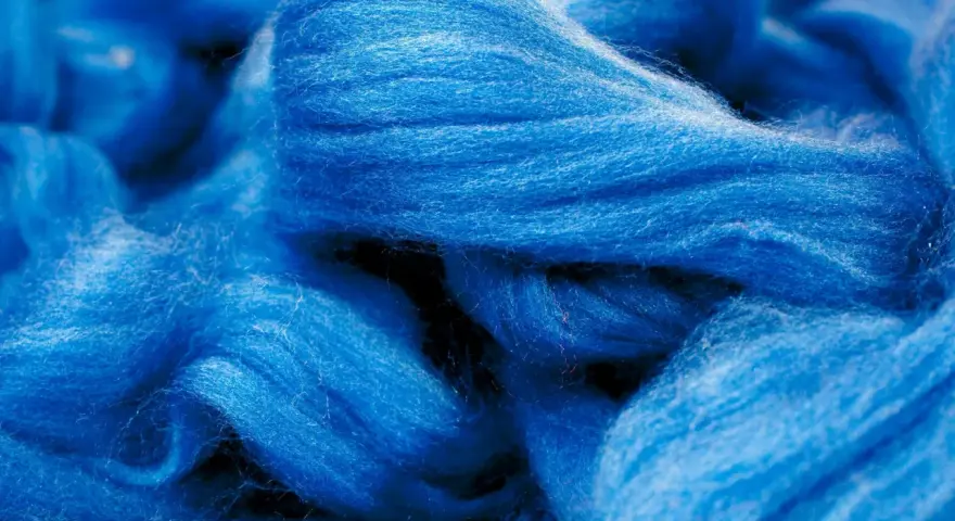 Leuchtend blaue Fasern, die an Wolle erinnern. Obwohl sie sich wie eine Naturfaser anfühlt, ist Viskose eine künstlich hergestellte Faser.