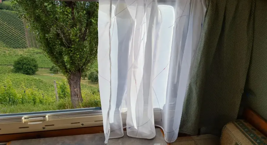 Leichte, transparente **Wohnwagen Gardinen Ideen** mit bunten Fäden vor einem Fenster mit Blick auf Weinberge.