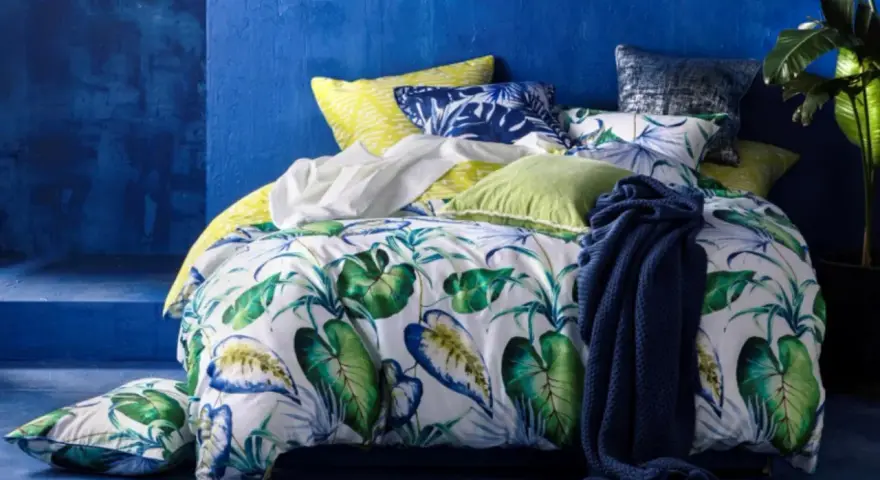 Ein tropisch gemustertes Bett mit Kissen in Blau und Grün. Für ein frisches Gefühl: wie oft Bettdecke wechseln?