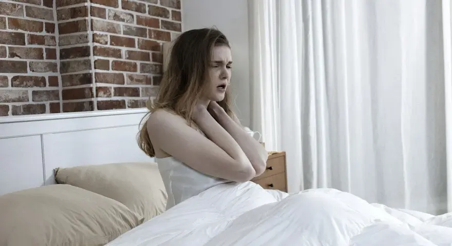 Junge Frau im Bett, die sich die Kehle hält, als ob das **Bett quietscht** und sie stört.