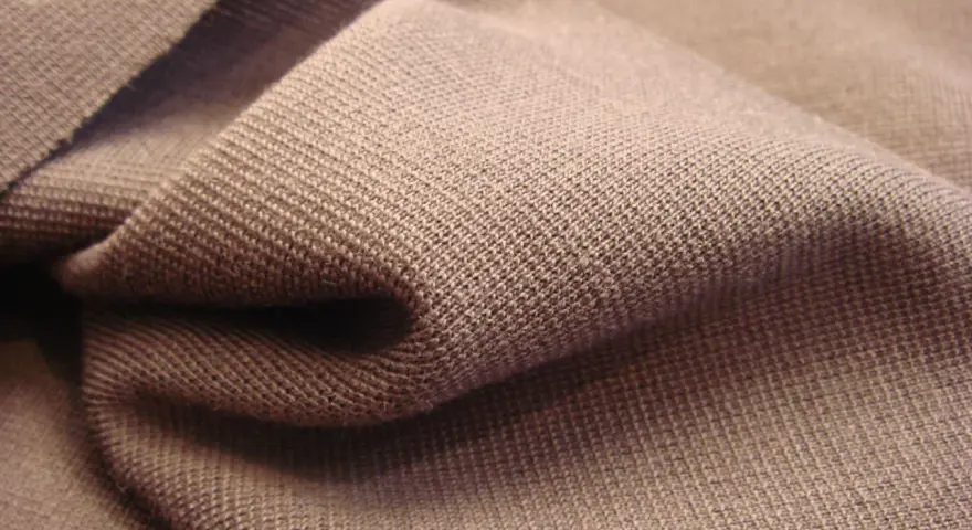 Braune Stofffalten, die die glatte, feine Struktur von Single Jersey zeigen. Dieses Material ist weich und dehnbar.