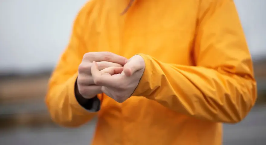 Person reibt sich die Hände unter einer leuchtend orangen Jacke. Ist Polyester warm? Ja, diese Jacke hält warm.