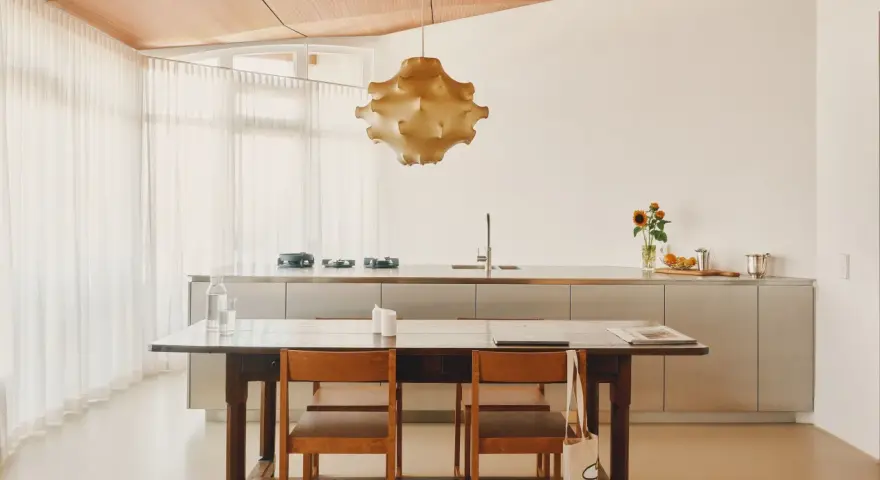 Ein Essbereich mit Holztisch und Stühlen, der den schwedischen Wohnstil verkörpert. Dahinter eine moderne Küche mit Edelstahlfronten und eine auffällige Hängelampe.